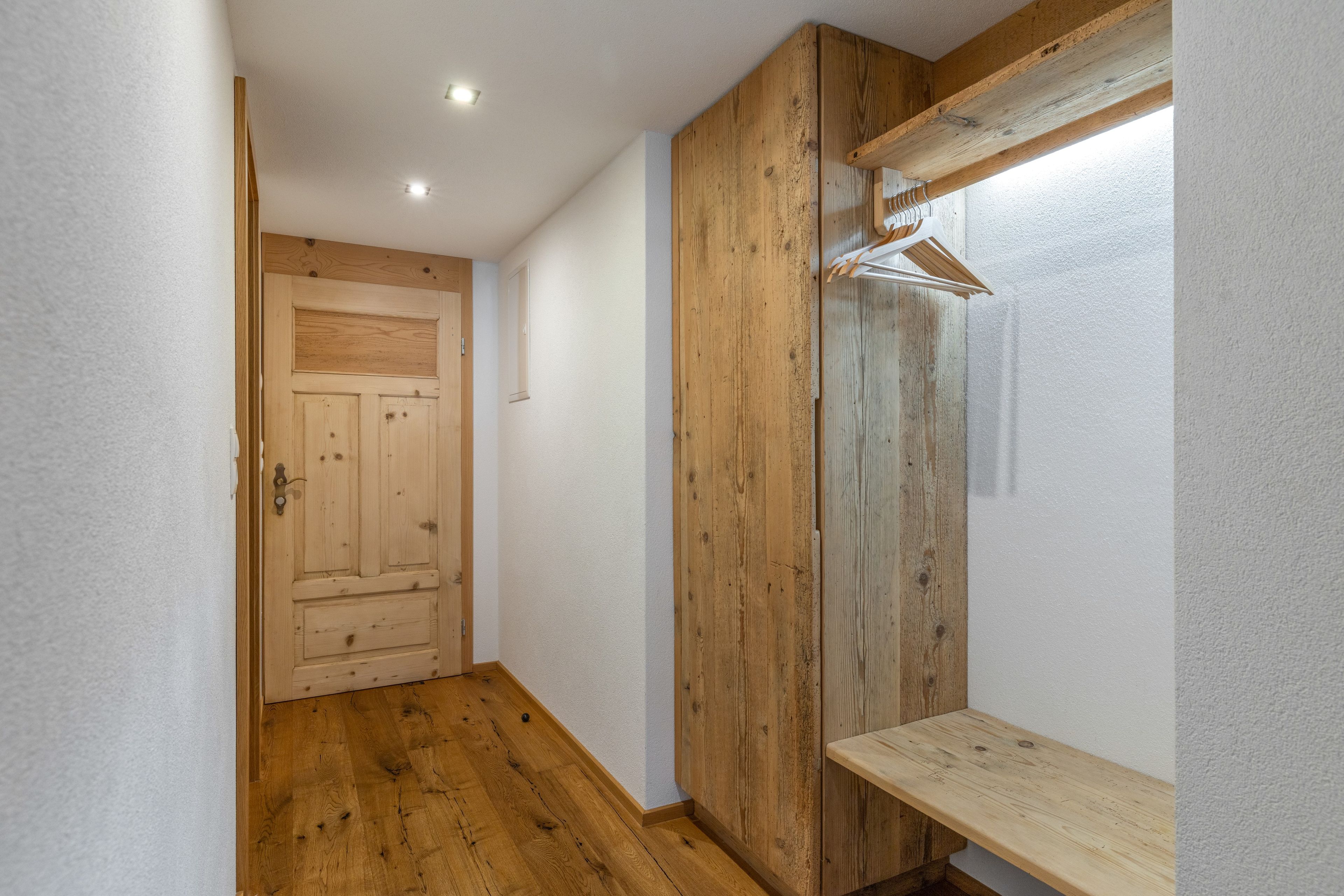 Ein Korridor mit Holzboden, einer Holztür und einem Holzschrank mit Spiegel.