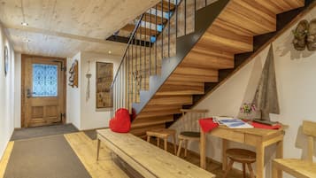 A wooden staircase with a modern design, a bench, a table with a vase of flowers, and a wooden door.