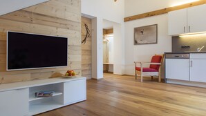 A modern living space with a flat-screen TV, wooden panel walls, a kitchen area, and a red chair.