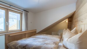 A bedroom with a sloped ceiling, a bed with patterned bedding, a window with curtains, and a wooden headboard.