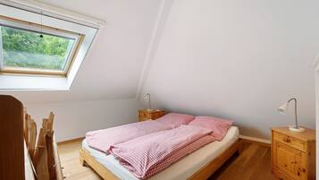 A bedroom with a sloped ceiling, a skylight, a wooden bed, a nightstand, and a desk with a chair.