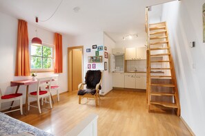 Ein Zimmer mit Esstisch, Stühlen, einem Sessel mit Felldecke, einer Holzleiter und einer Küchenzeile.