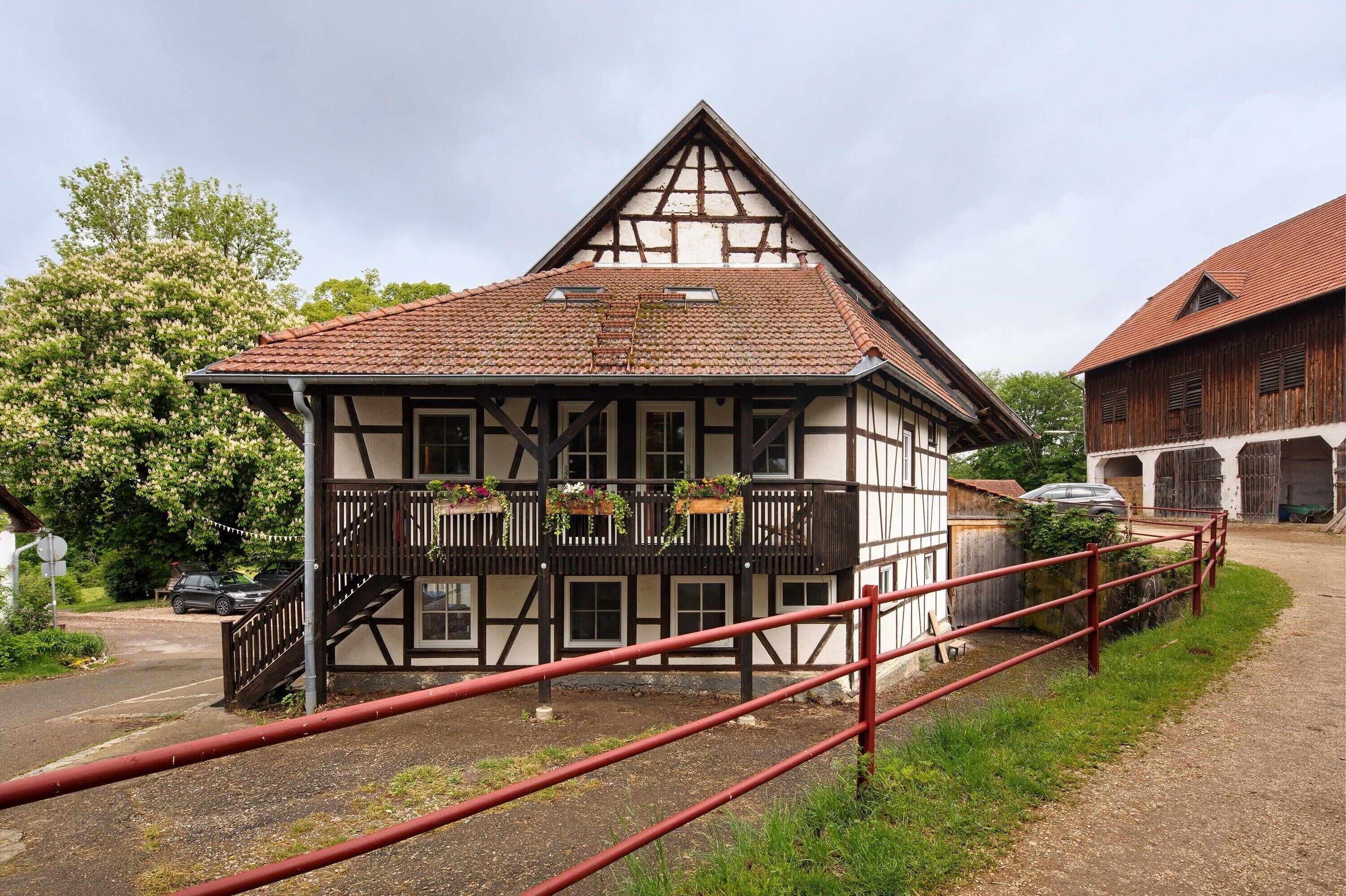 Una casa tradicional de entramado de madera con balcón, escaleras y una cerca de metal roja.