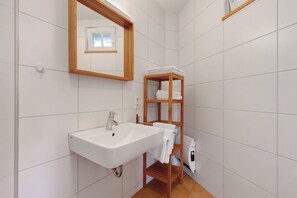 A bathroom with a white sink, wooden shelves, and a mirror. - Apartment 'Stallblick' with Shared Terrace, Shared Garden and Wi-Fi (Bad Urach)