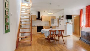 A kitchen with wooden cabinets, a dining table with chairs, a ladder, and a TV on a stand. - Apartment 'Stallblick' with Shared Terrace, Shared Garden and Wi-Fi (Bad Urach)