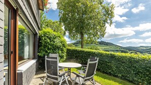 Une terrasse extérieure avec une table et des chaises, une vue sur un paysage verdoyant et luxuriant, et un bâtiment doté de grandes fenêtres.