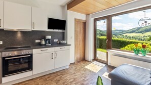 Une cuisine moderne dotée d’appareils électroménagers intégrés, d’un téléviseur à écran plat et d’une grande fenêtre offrant une vue sur un paysage verdoyant.