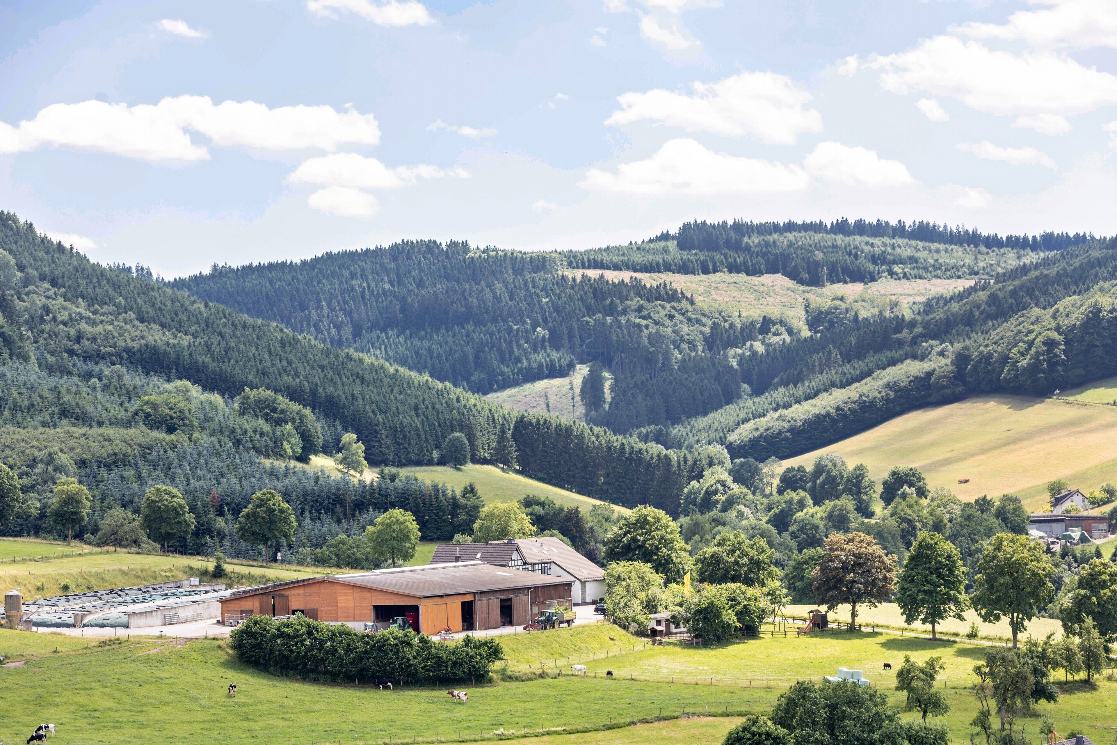 A rural landscape with a large building, possibly a farm or barn, surrounded by green fields and hills.