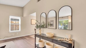A modern living room with a dark console table, three mirrors, and a potted plant.