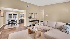 A living room with a beige sofa, a wooden coffee table, and a dining area with a table and chairs.