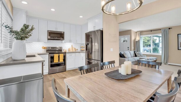 A modern kitchen with white cabinets, stainless steel appliances, and a dining area with a wooden table and chairs.
