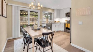 A modern kitchen with white cabinets, a stainless steel refrigerator, and a dining area with a wooden table and chairs.