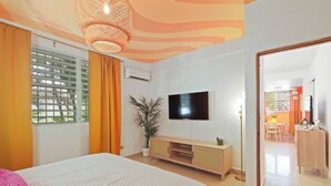 Un dormitorio con cama, televisor, planta y ventana con cortinas.