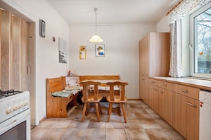 Une cuisine compacte avec un coin repas, des placards en bois, une cuisinière et une fenêtre donnant sur un paysage agréable.