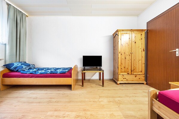 Une chambre avec un lit, un téléviseur posé sur une petite table et une armoire en bois.