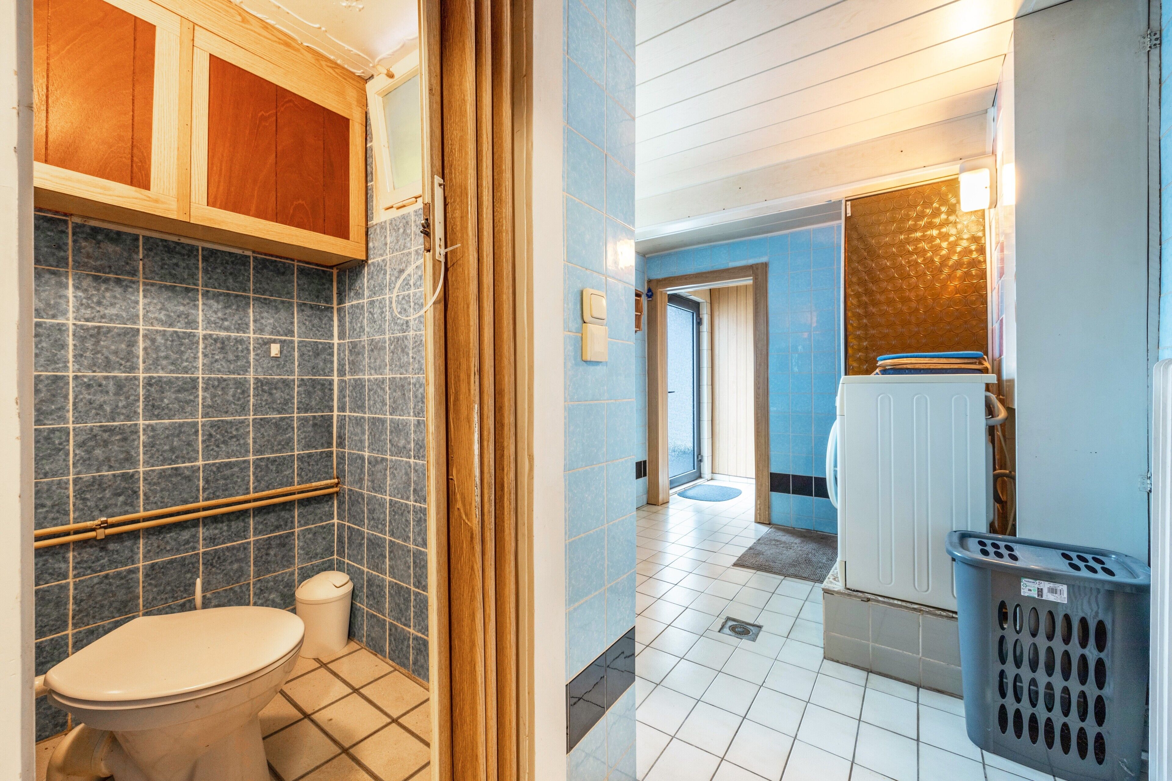 Un baño con inodoro, un cubo de basura, un armario de madera y una cesta de ropa.