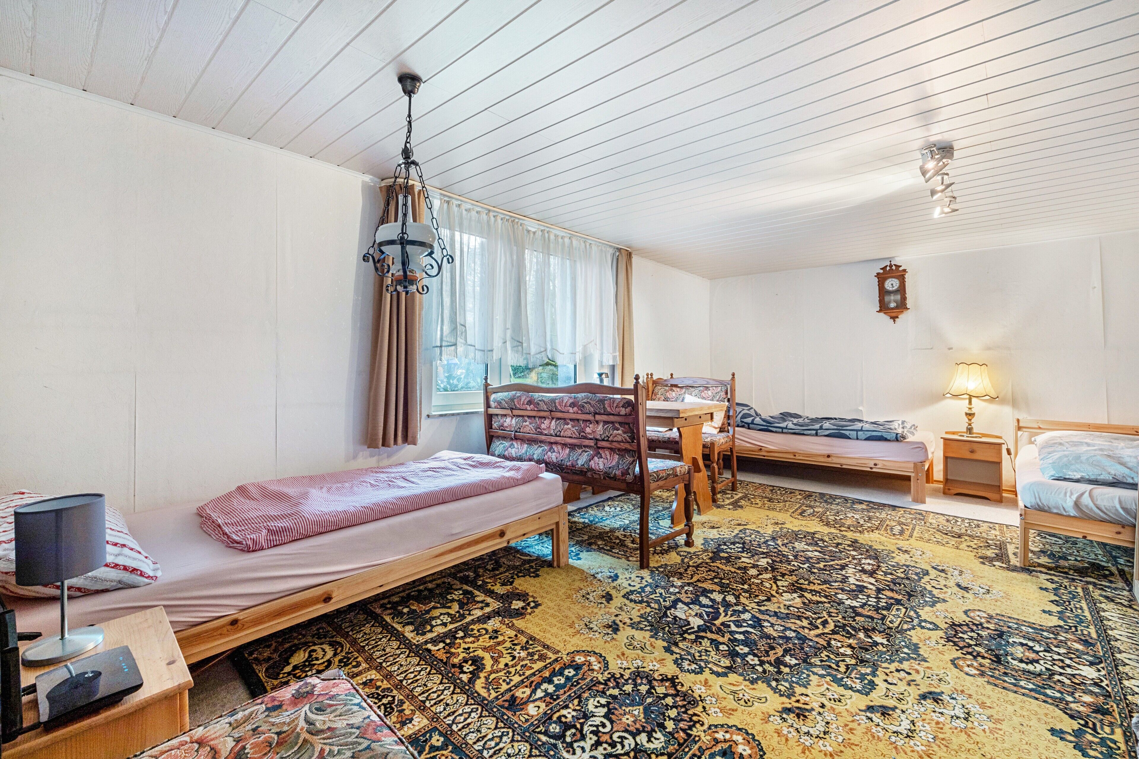 A room with a bed, a desk, a chair, a small table, a lamp, and a clock on the wall.