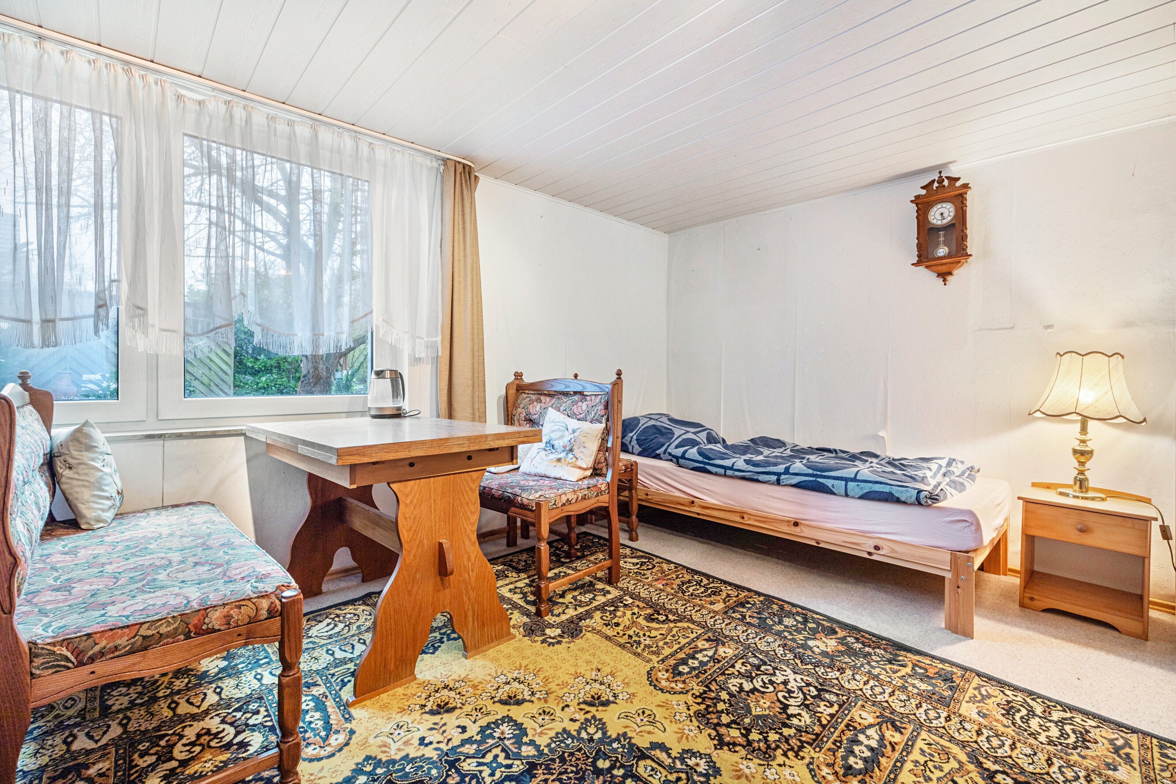 Ein Zimmer mit einem Bett, einem Schreibtisch, einem Stuhl, einer Lampe und einem Vorhangfenster.