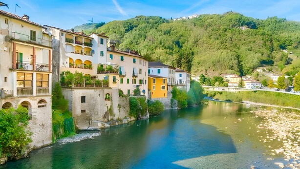 A river with buildings on one side, a bridge, and a hill in the background.