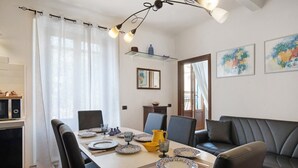 A dining area with a table set for four, chairs, a sofa, a kitchen area with a microwave, and artwork on the walls.