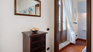 A room with a wooden dresser, a mirror, and a door leading to a balcony with a white curtain.