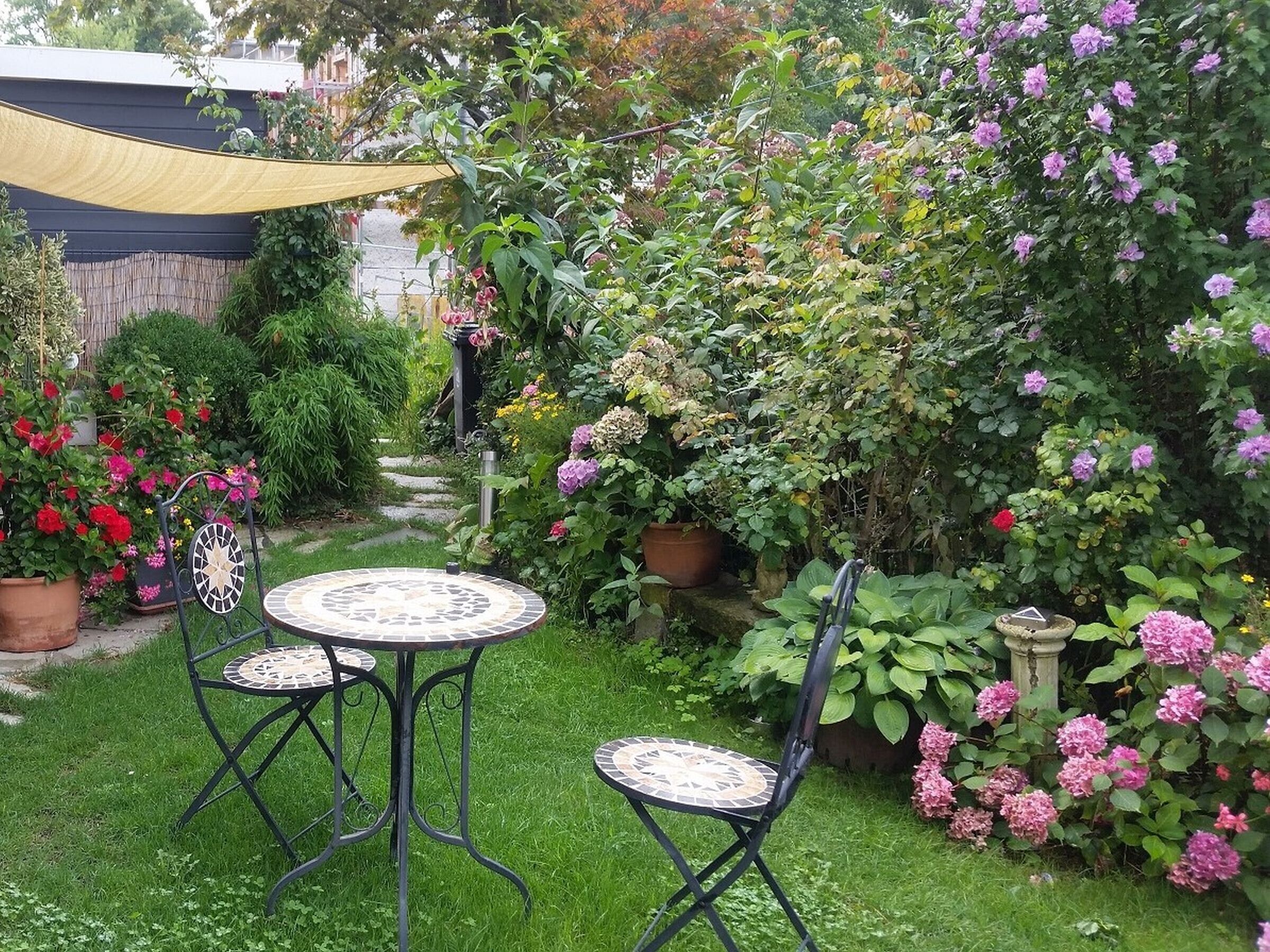 A garden with two round tables and chairs, surrounded by various potted plants and flowers.