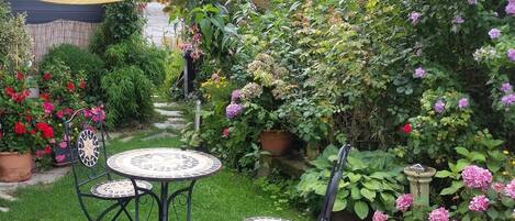 A garden with two round tables and chairs, surrounded by various potted plants and flowers.