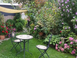 A garden with two round tables and chairs, surrounded by various potted plants and flowers.