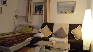 Een kamer met een bed, een slaapbank, een glazen salontafel, een lamp, een spiegel en een raam met gordijnen.