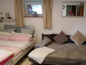 A bedroom with two beds, a window with curtains, a mirror, and a shelf with decorative items.
