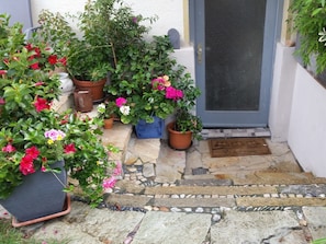 A stone-paved entrance with potted plants and a door with a screen.