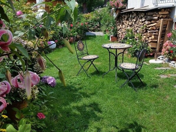 Un jardín con un muro de piedra, un banco de madera y una mesa de metal con sillas.