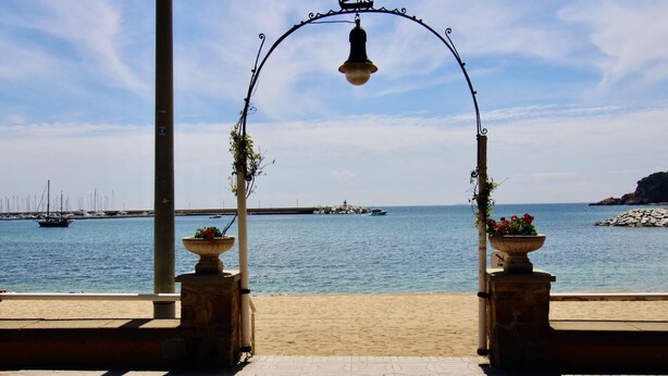 An outdoor seating area with a view of the sea, featuring a decorative archway with a bell and a ship silhouette. - Loft in the center 100 meters from the beach (Sant Feliu de Guíxols)