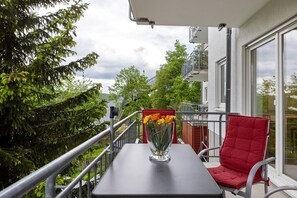 Un balcon avec une table, une chaise rouge et un vase rempli de fleurs.