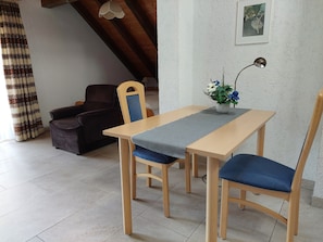 Un comedor con una mesa de madera, sillas con cojines azules, un camino de mesa gris, un jarrón de flores y un cuadro colgado en la pared.