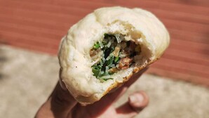 A hand holding a half-eaten dumpling with visible filling. - Lata Hotel (Nuku'alofa)