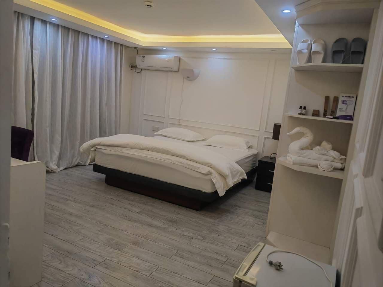 Un dormitorio moderno con una cama grande, una mesita de noche, un armario y una estantería con toallas y artículos de aseo.