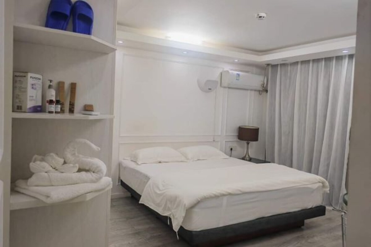 A hotel room with a bed, a shelf with toiletries, and a window with curtains.