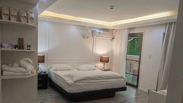 A modern bedroom with a large bed, a bedside table, a wardrobe, and a balcony with a glass door. - Lata Hotel (Nuku'alofa)