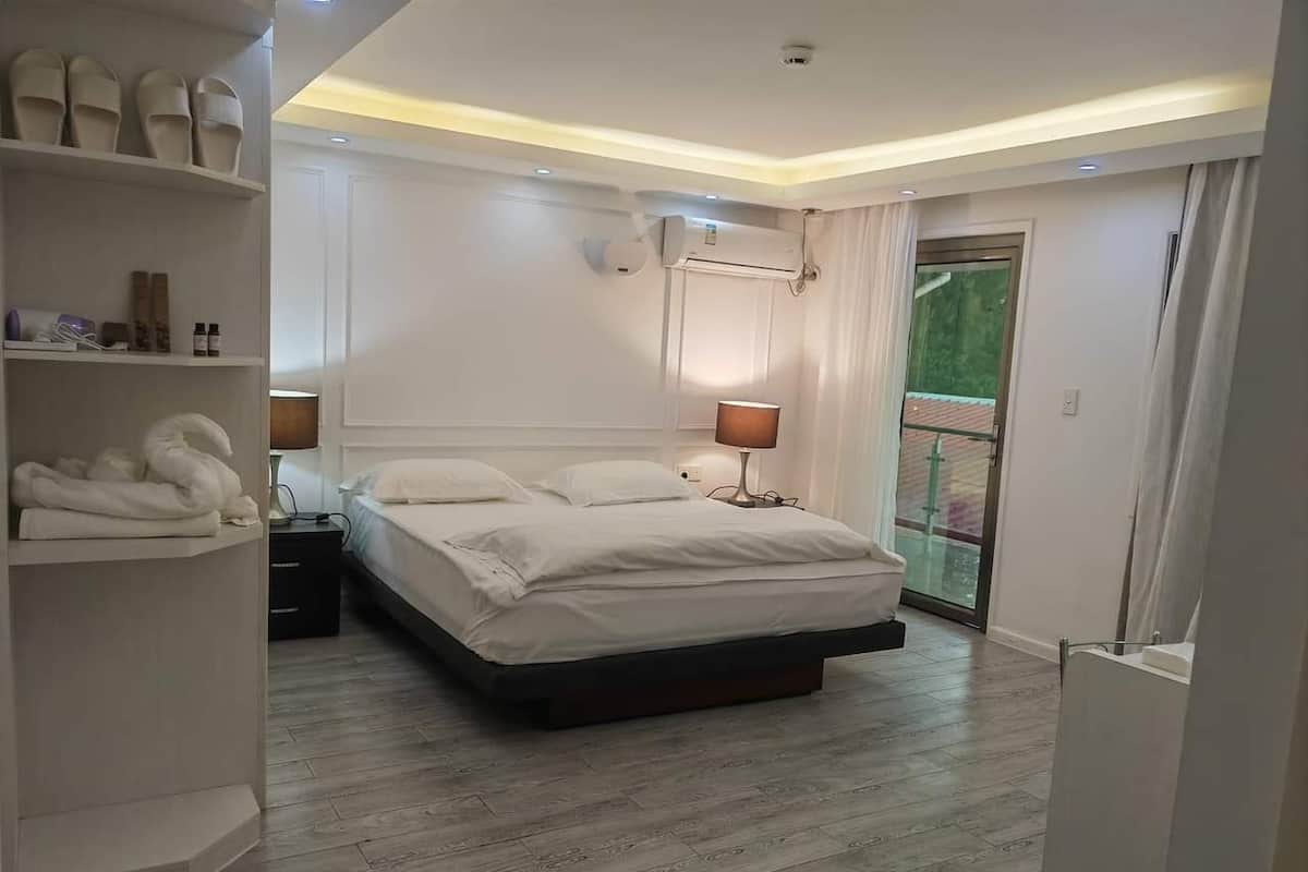 Un dormitorio moderno con una cama grande, una mesita de noche, un armario y un balcón con puerta de vidrio.