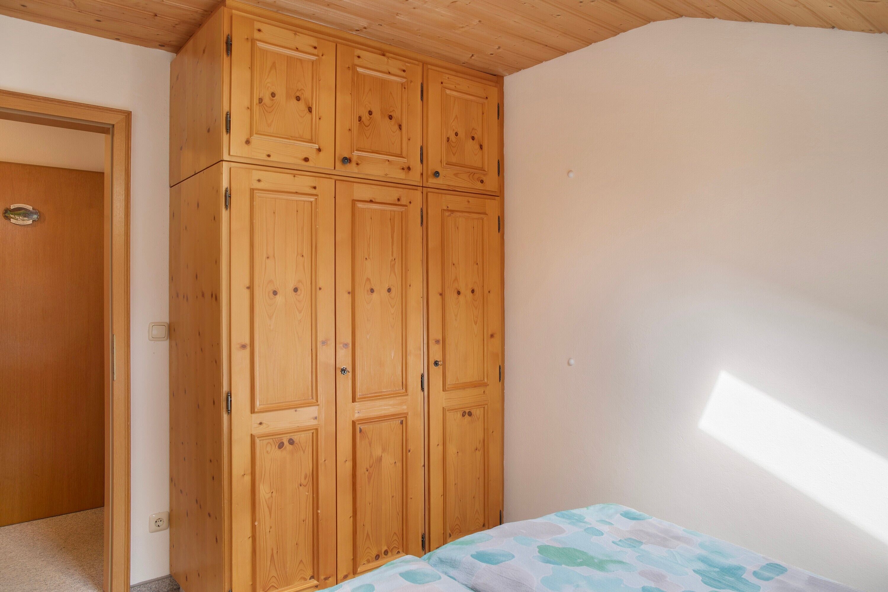 A bedroom with a wooden wardrobe, a bed with a patterned bedspread, and a sloped ceiling.