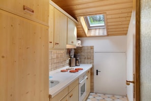 A compact kitchen with wooden cabinets, a white countertop, a built-in oven, and a small window.
