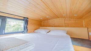 A wooden cabin room with a bed, a window with curtains, and a view of greenery outside. - La Casa Errante 3 by Tiny Away (Castilenti)