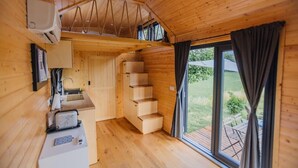 A wooden cabin interior with a kitchen area, a staircase, and a large window with curtains. - La Casa Errante 3 by Tiny Away (Castilenti)