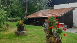Un edificio rústico de madera con techo de tejas, rodeado de un jardín cuidado con plantas en macetas y un banco de madera.