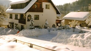 A two-story chalet with a sloped roof, wooden balconies, and a snow-covered landscape.