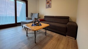 Un salón con un sofá, una mesa con una botella y vasos, y una ventana con persianas.