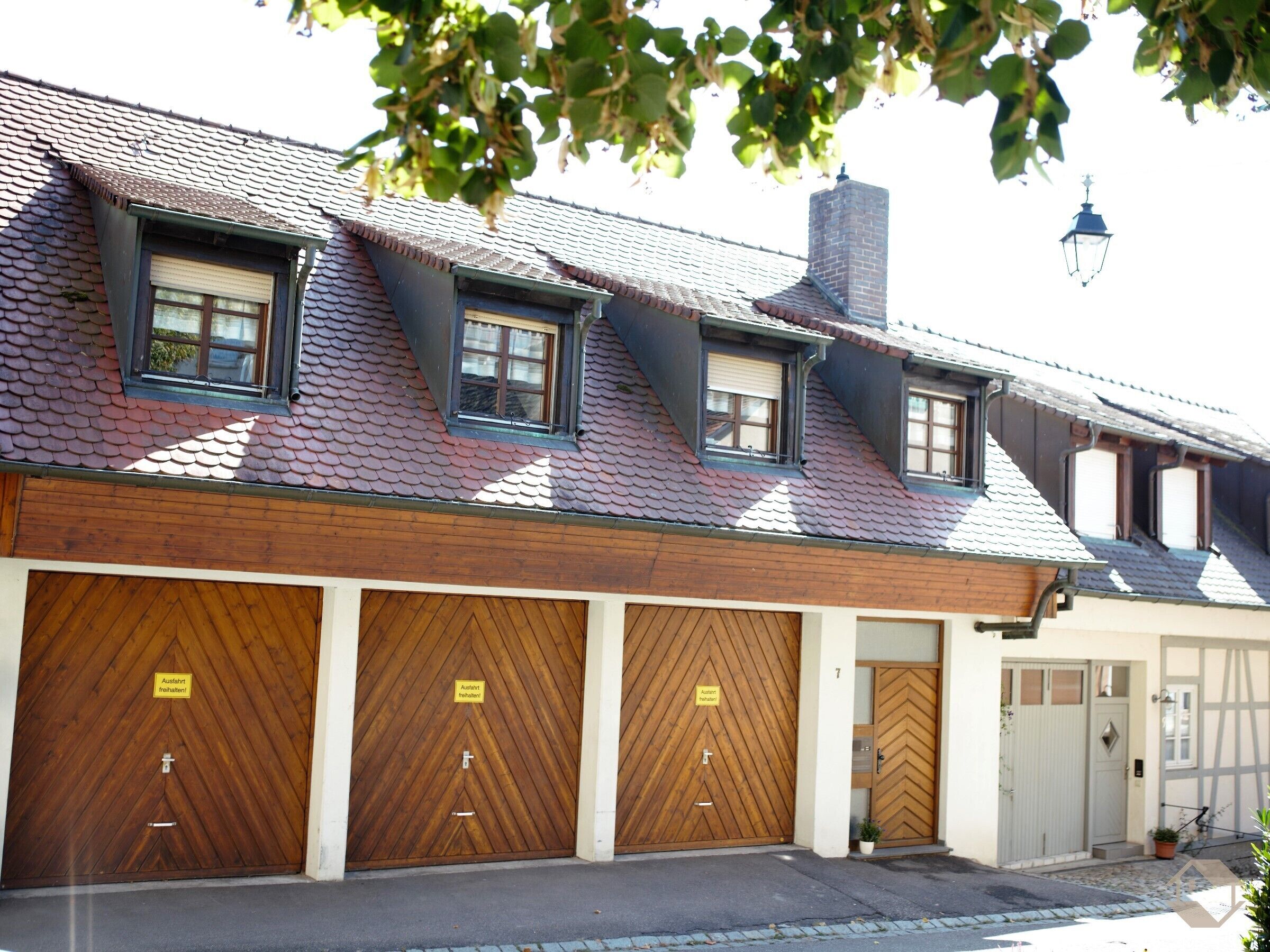 A building with a sloped roof, multiple windows, and three wooden garage doors with signs.