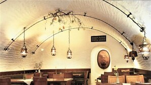 Un comedor interior con mesas y sillas de madera, faroles colgantes y un techo abovedado blanco.