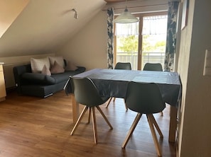 Ein Essbereich mit Tisch, Stühlen und einer Couch in einem Raum mit Holzboden und schrägverdeckter Decke.